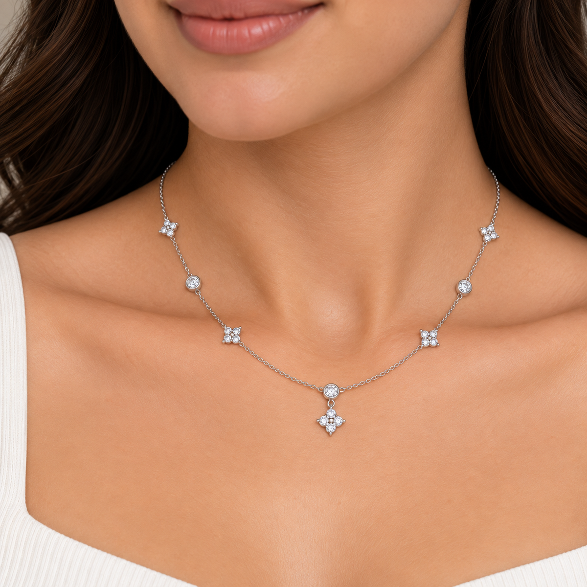 A close-up of a woman wearing a delicate silver-toned necklace with five small floral clusters spaced along a fine chain and a larger matching pendant hanging at the center, photographed against her neck and upper chest.