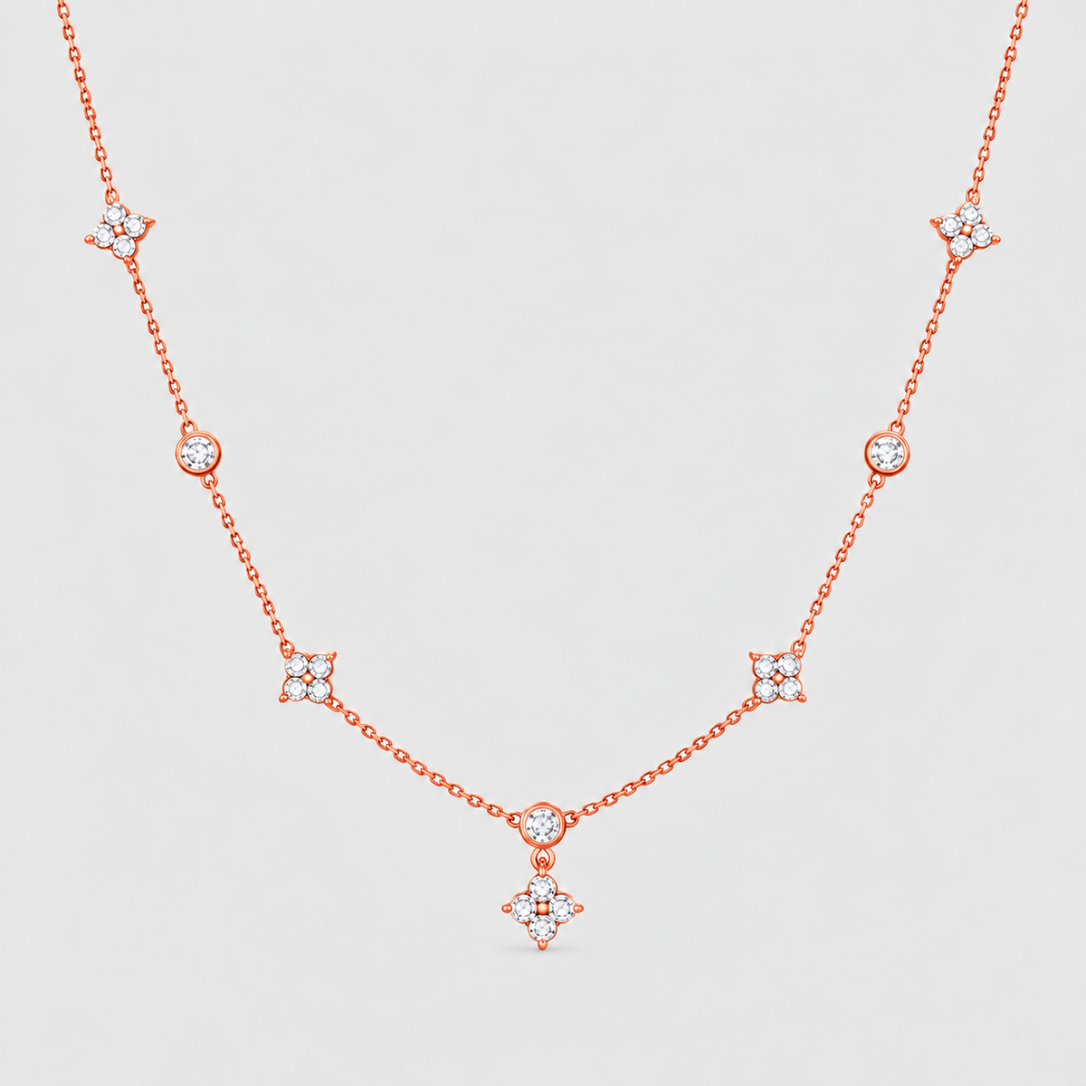 A delicate rose gold chain necklace featuring multiple small diamond-like star and oval motifs spaced along the chain, displayed against a light gray background.