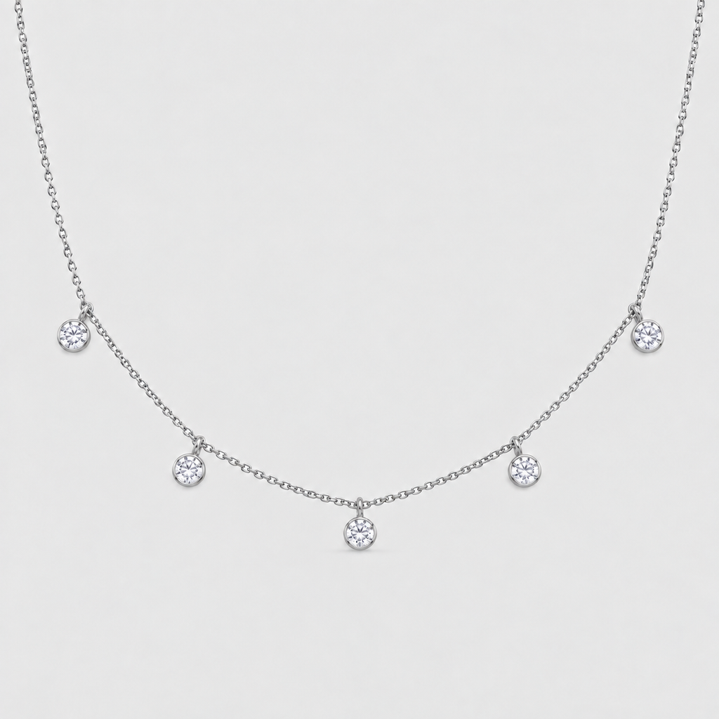 A delicate silver-toned chain necklace featuring five small, bezel-set round clear gemstones spaced along the chain, displayed against a light gray background.