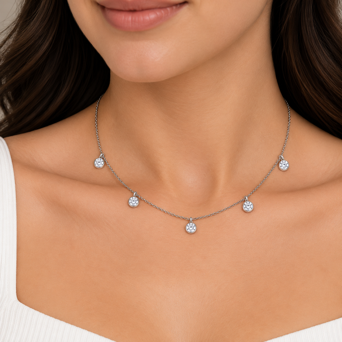 A close-up of a woman wearing a delicate silver-toned necklace with five small round clear gemstone pendants, shown against her neck and upper chest.