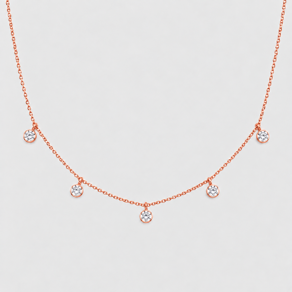 A delicate rose gold necklace featuring five small, round clear gemstones spaced along the chain, displayed against a light gray background.