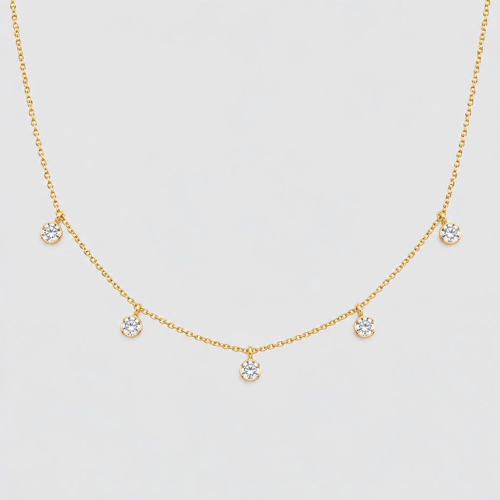 A delicate gold chain necklace featuring five small, round bezel-set clear gemstones spaced evenly along the chain, displayed against a light gray background.