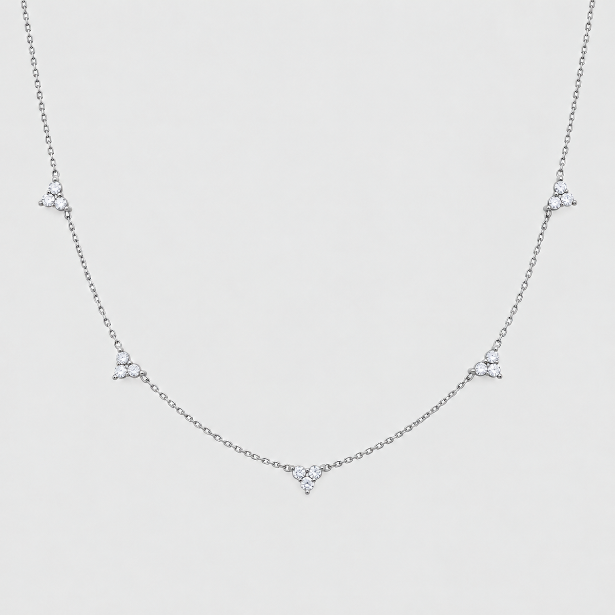 A delicate silver chain necklace featuring five small, clear triangular crystal clusters spaced evenly along the chain, displayed against a light gray background.