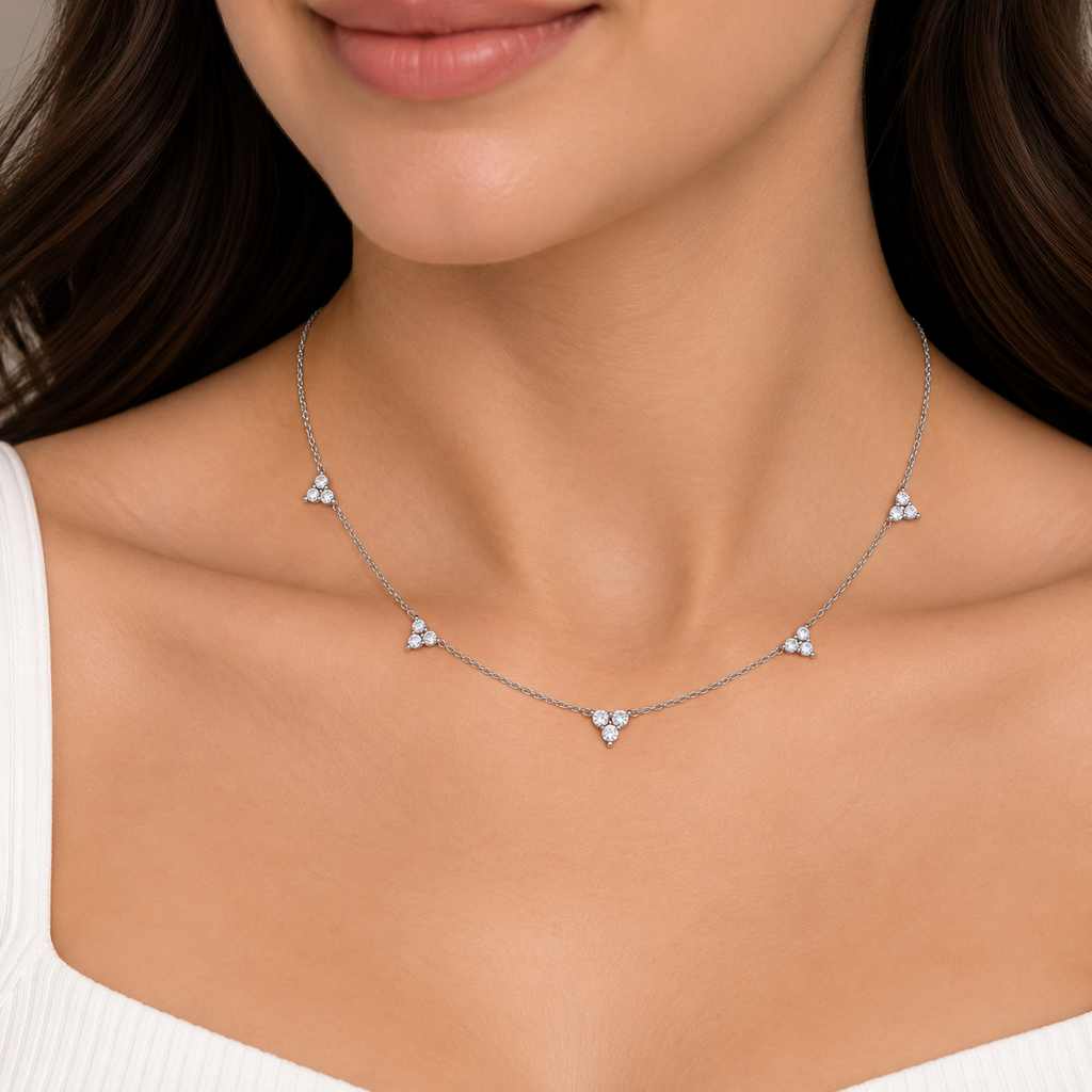 A close-up of a woman wearing a delicate silver necklace with small cluster diamond pendants at the center of the chest and along the chain.