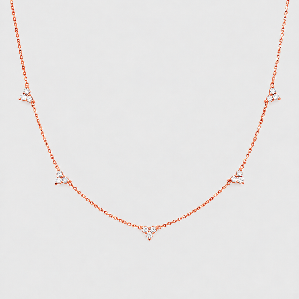 A delicate rose gold chain necklace featuring five small triangular clusters of clear stones spaced along the chain, displayed against a light gray background.