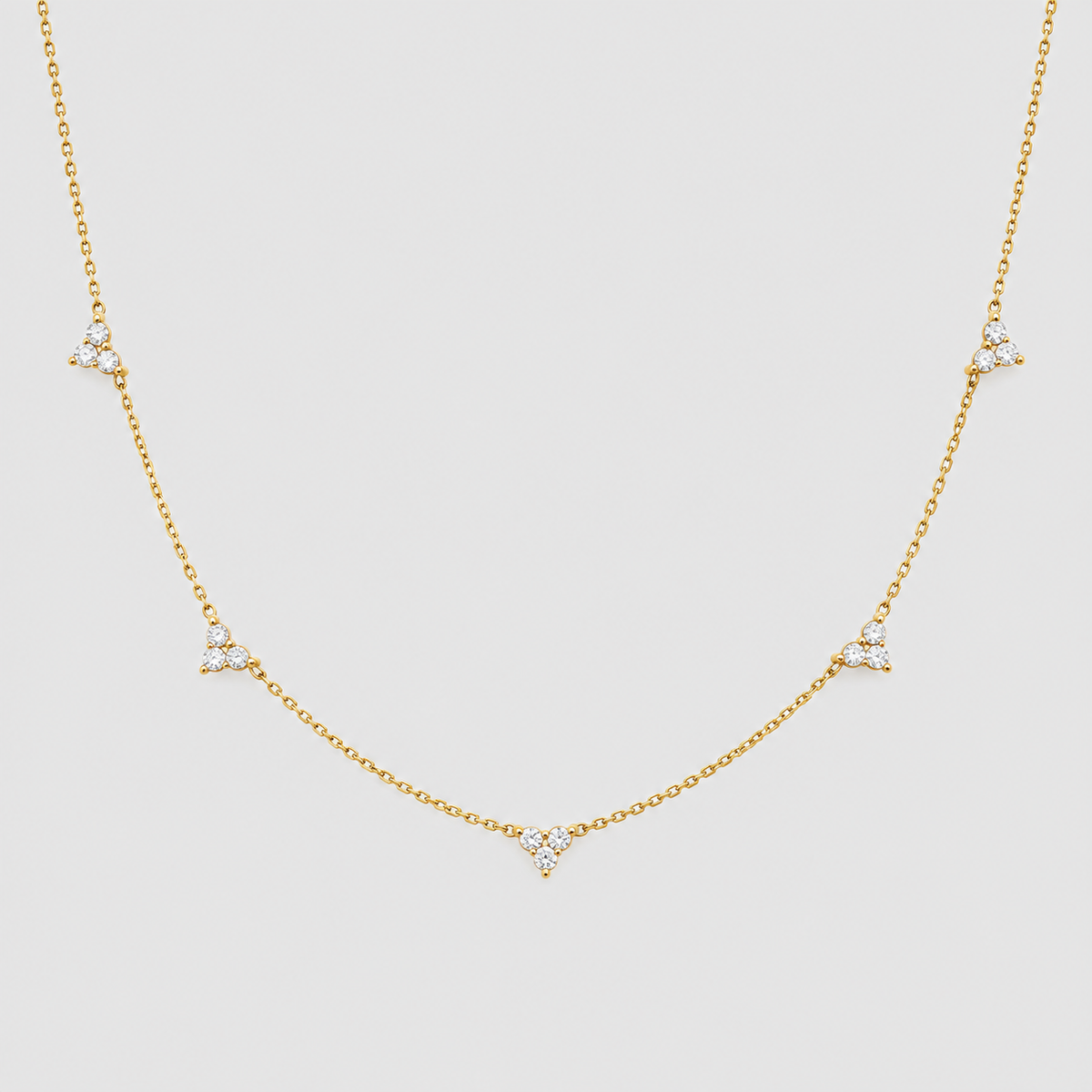 A delicate gold chain necklace featuring five small triangular diamond clusters spaced along the chain, displayed against a solid light gray background.