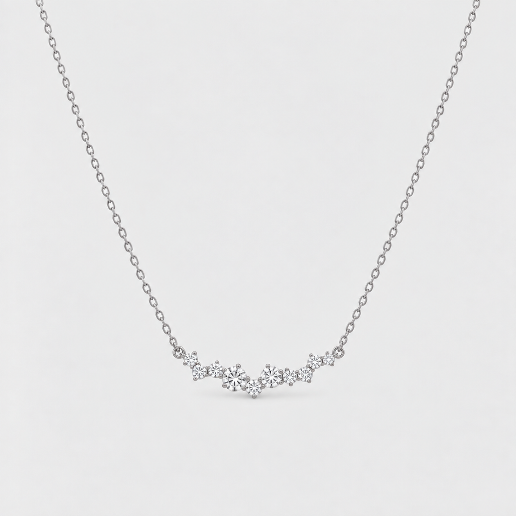 A delicate silver chain necklace featuring a small, wavy cluster of clear gemstones at the center, displayed against a light gray background.