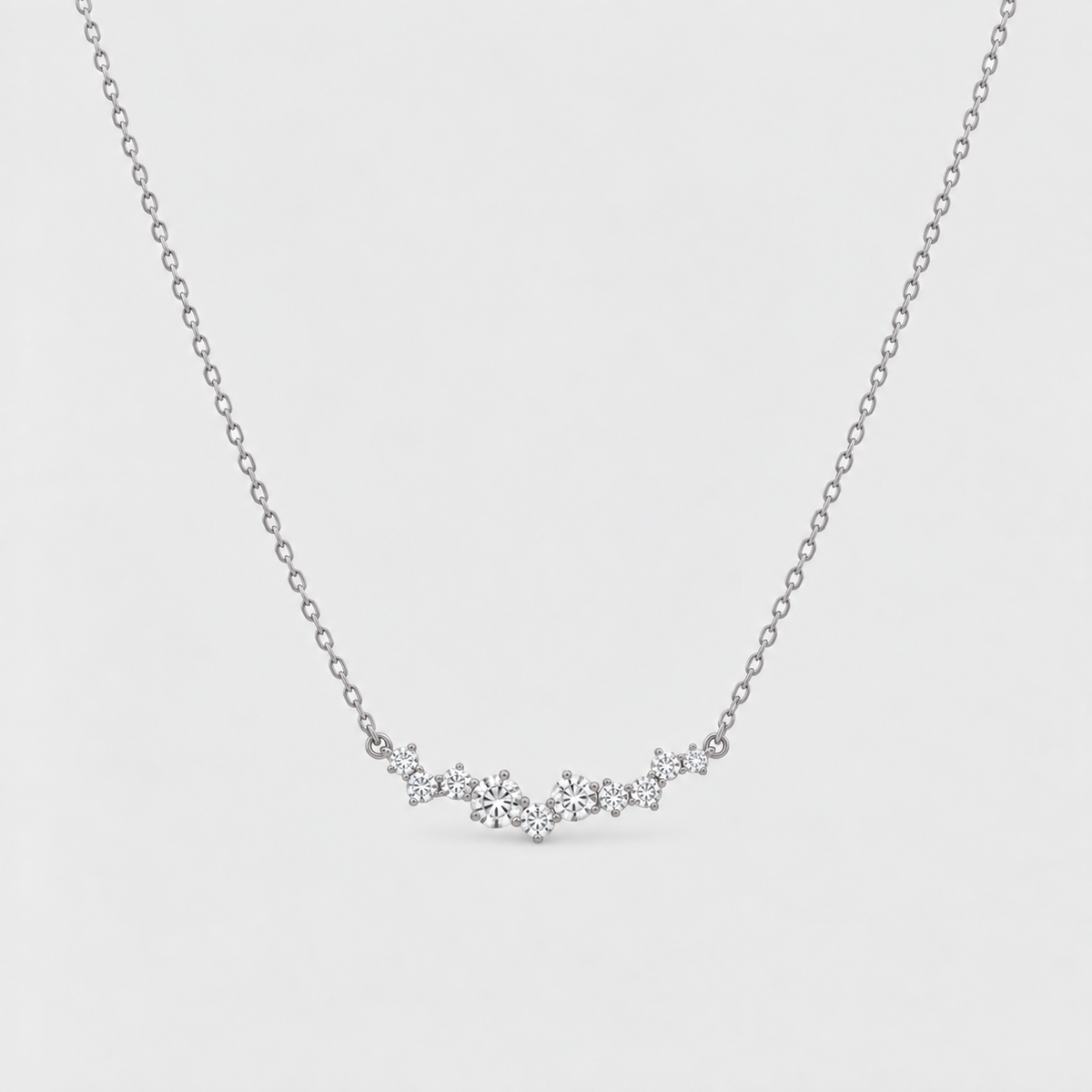 A delicate silver chain necklace featuring a small, wavy cluster of clear gemstones at the center, displayed against a light gray background.