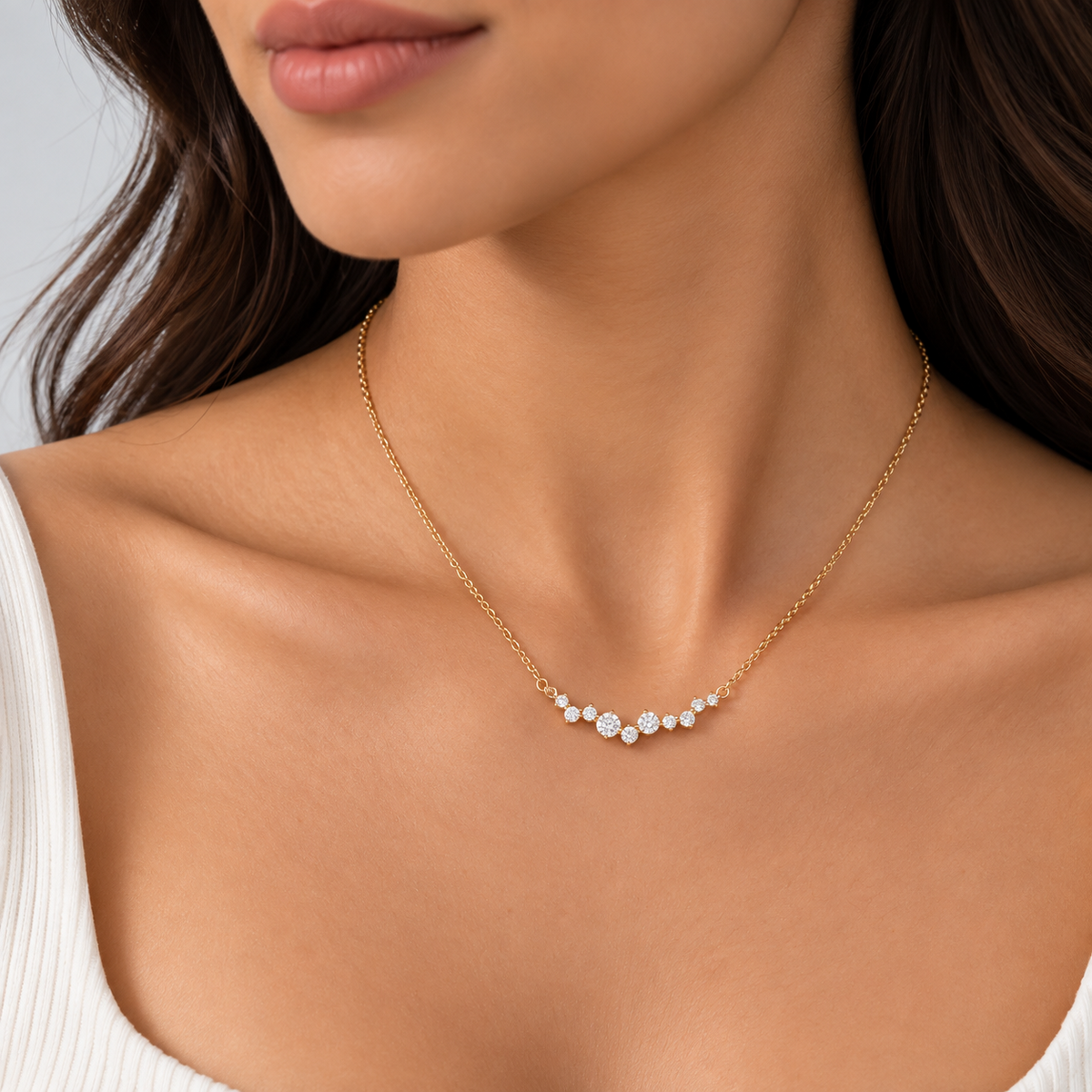 A close-up lifestyle shot of a model wearing a delicate gold necklace with a curved row of small clear gemstones at the center of the chest.