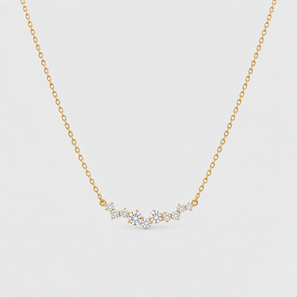 A delicate gold chain necklace featuring a small, wavy bar of clear gemstones in a prong setting, displayed against a light gray background.