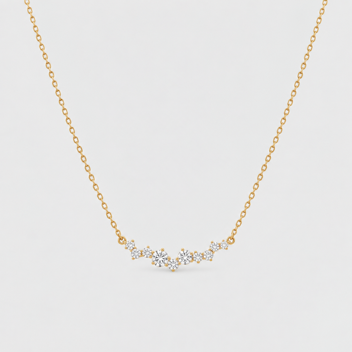 A delicate gold chain necklace featuring a small, wavy bar of clear gemstones in a prong setting, displayed against a light gray background.