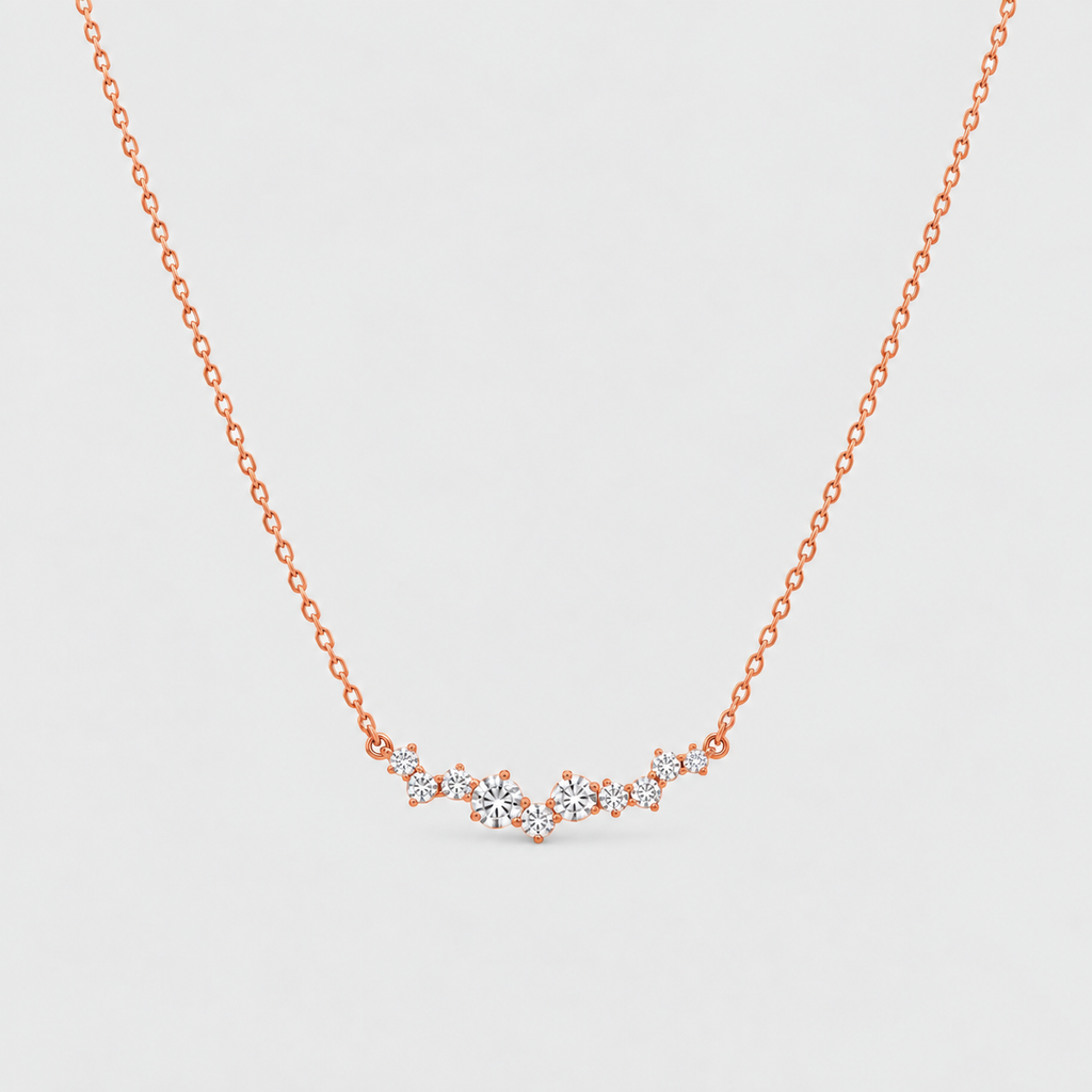 A delicate rose gold chain necklace featuring a small, wavy cluster of clear gemstones at the center, displayed against a clean, light gray background.