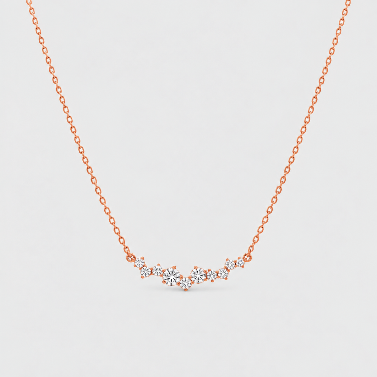 A delicate rose gold chain necklace featuring a small, wavy cluster of clear gemstones at the center, displayed against a clean, light gray background.