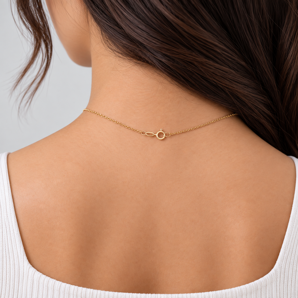 A delicate gold chain necklace with a small infinity symbol charm, shown worn on the back of a woman's neck over a white ribbed top.