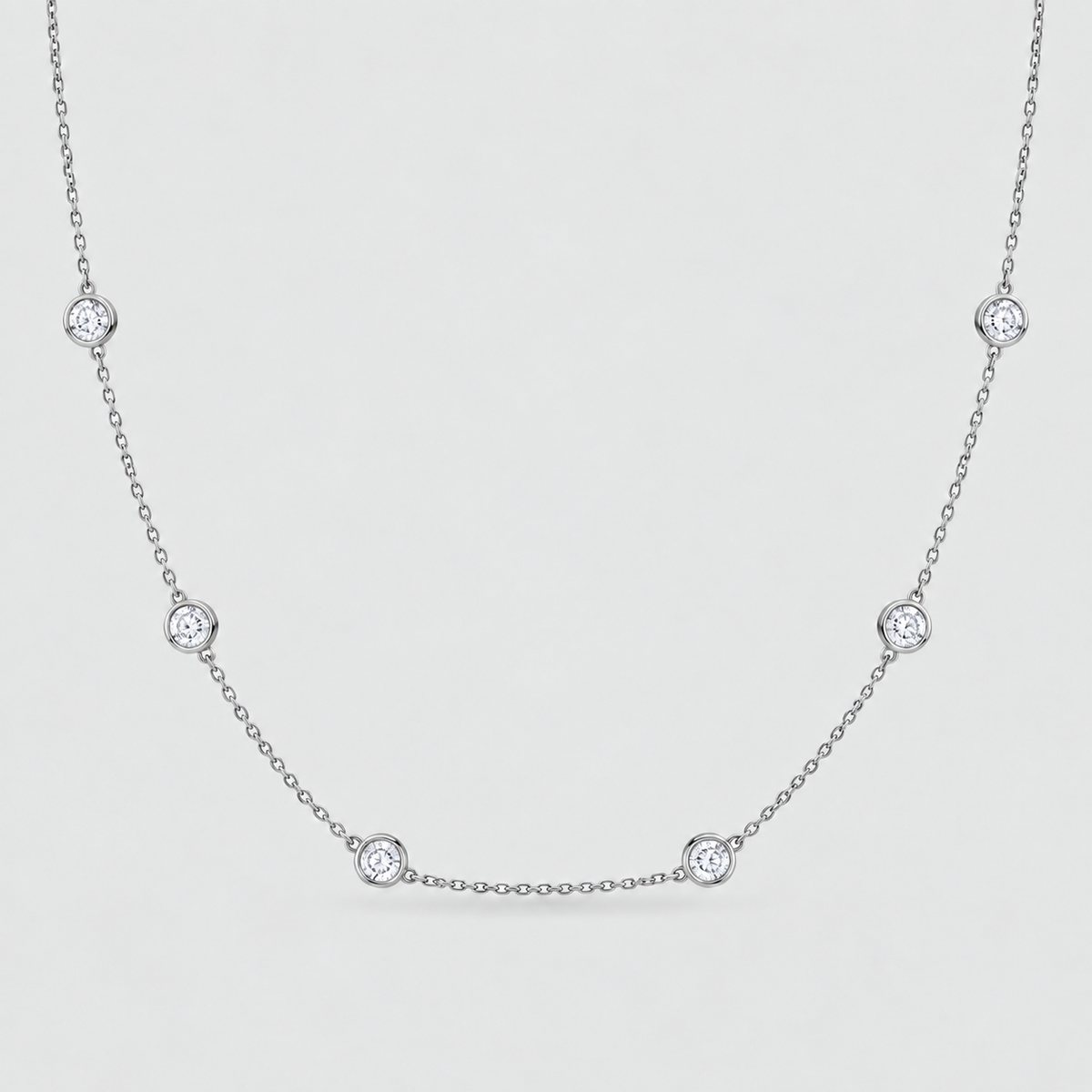 A delicate silver chain necklace featuring five evenly spaced round bezel-set clear gemstones on a light gray background.