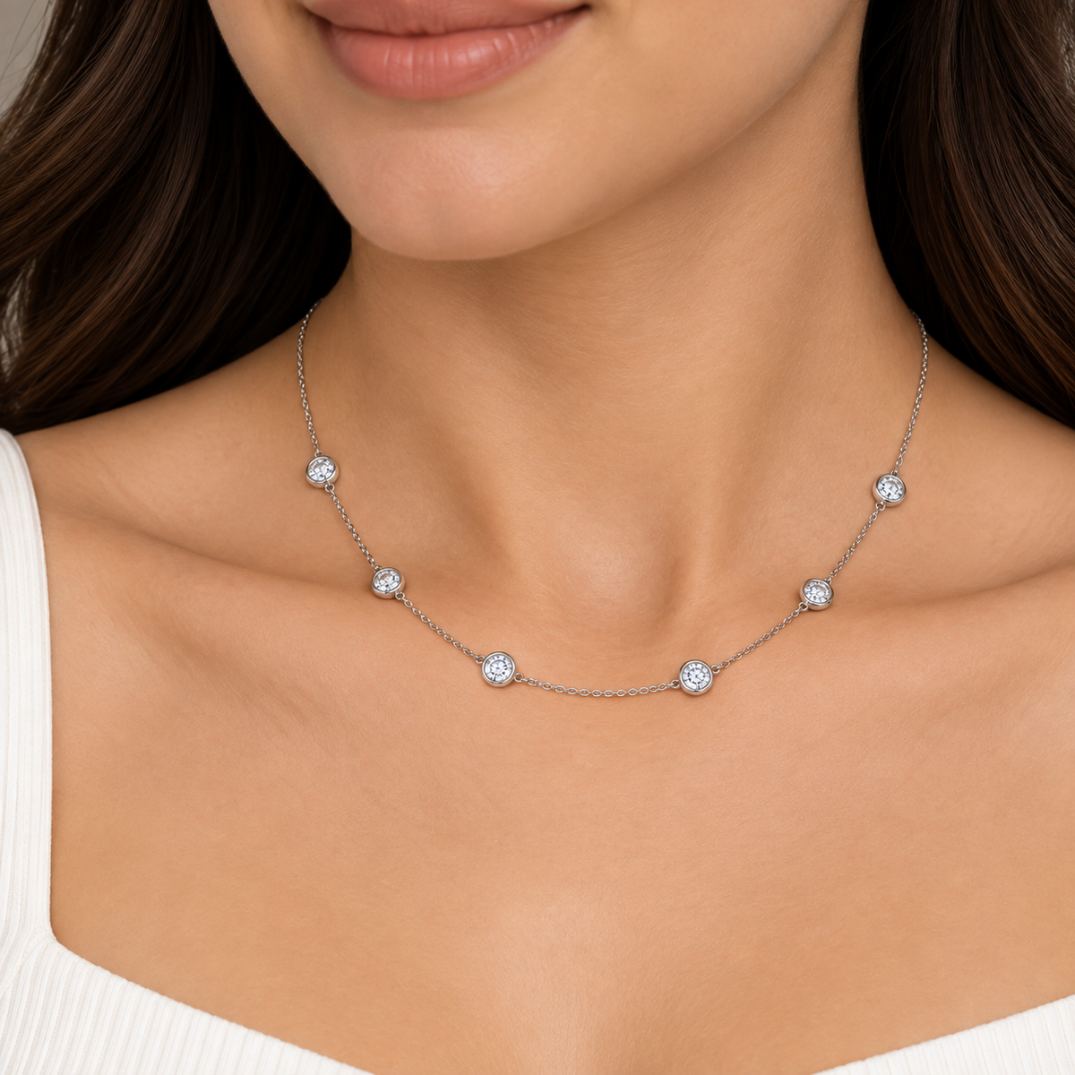 A close-up of a woman wearing a delicate silver chain necklace with five small, round, diamond-like bezel-set stones spaced evenly along the chain.
