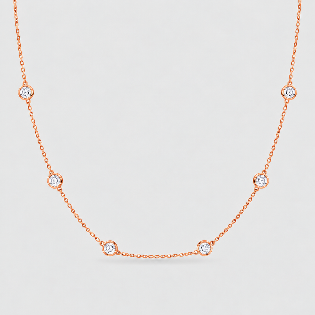 A delicate rose gold chain necklace featuring seven small, bezel-set round clear gemstones spaced evenly along the chain, displayed against a light gray background.