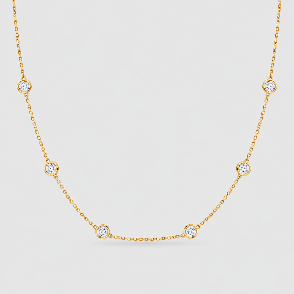 A delicate yellow gold chain necklace featuring five evenly spaced round bezel-set clear gemstones on a light gray background.
