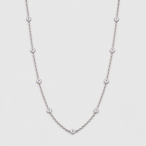 A delicate silver chain necklace featuring seven small, evenly spaced round clear gemstones, displayed against a light gray background.
