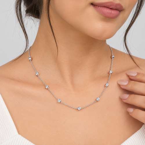 A close-up of a woman wearing a delicate silver necklace with small clear gemstone beads spaced along the chain. The necklace is shown on her neck and upper chest, with her hand resting near one side of the necklace.
