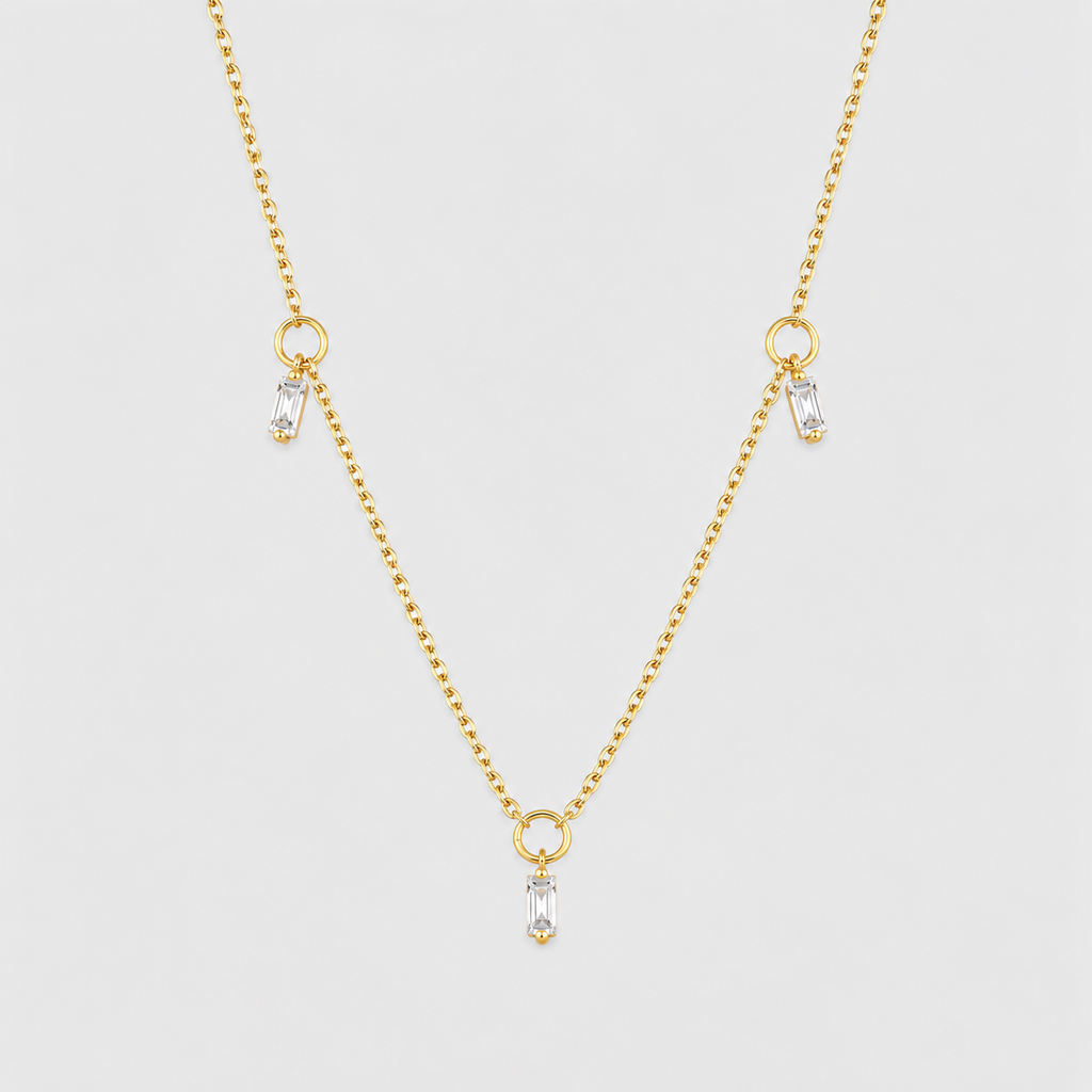A delicate gold chain necklace featuring three small teardrop-shaped clear crystals hanging from gold rings at the center and two side locations, displayed against a light gray background.