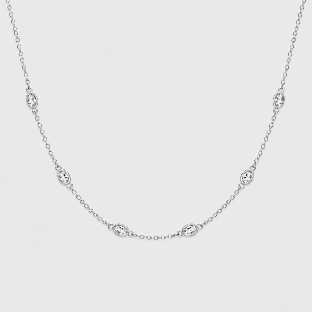 A delicate silver chain necklace featuring five small oval bezel-set clear stones, displayed against a clean, light gray background.
