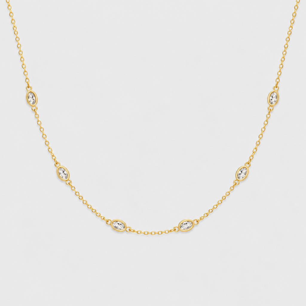 A delicate yellow gold chain necklace featuring five small oval bezel-set clear stones spaced evenly along the chain, displayed against a light gray background.