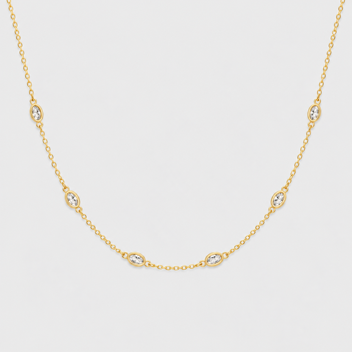 A delicate yellow gold chain necklace featuring five small oval bezel-set clear stones spaced evenly along the chain, displayed against a light gray background.