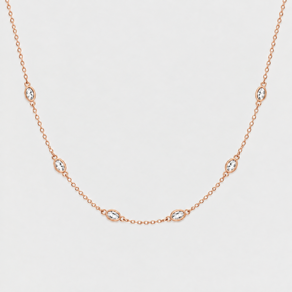 A delicate rose gold chain necklace featuring seven small oval bezel-set clear stones spaced evenly along the chain, displayed against a clean light gray background.