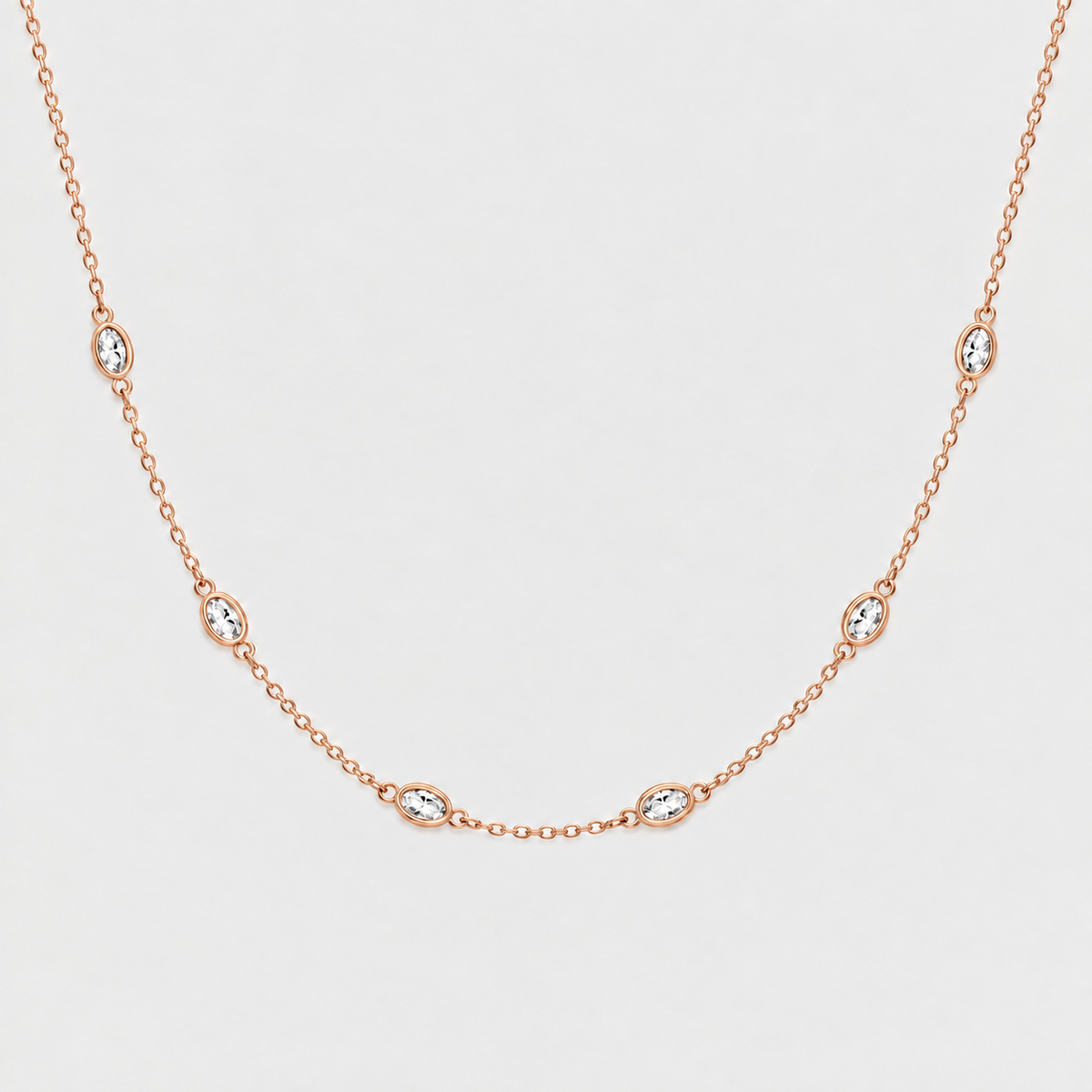 A delicate rose gold chain necklace featuring seven small oval bezel-set clear stones spaced evenly along the chain, displayed against a clean light gray background.