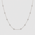 A delicate silver chain necklace featuring seven small, evenly spaced round bezel-set clear gemstones, displayed against a solid light gray background.