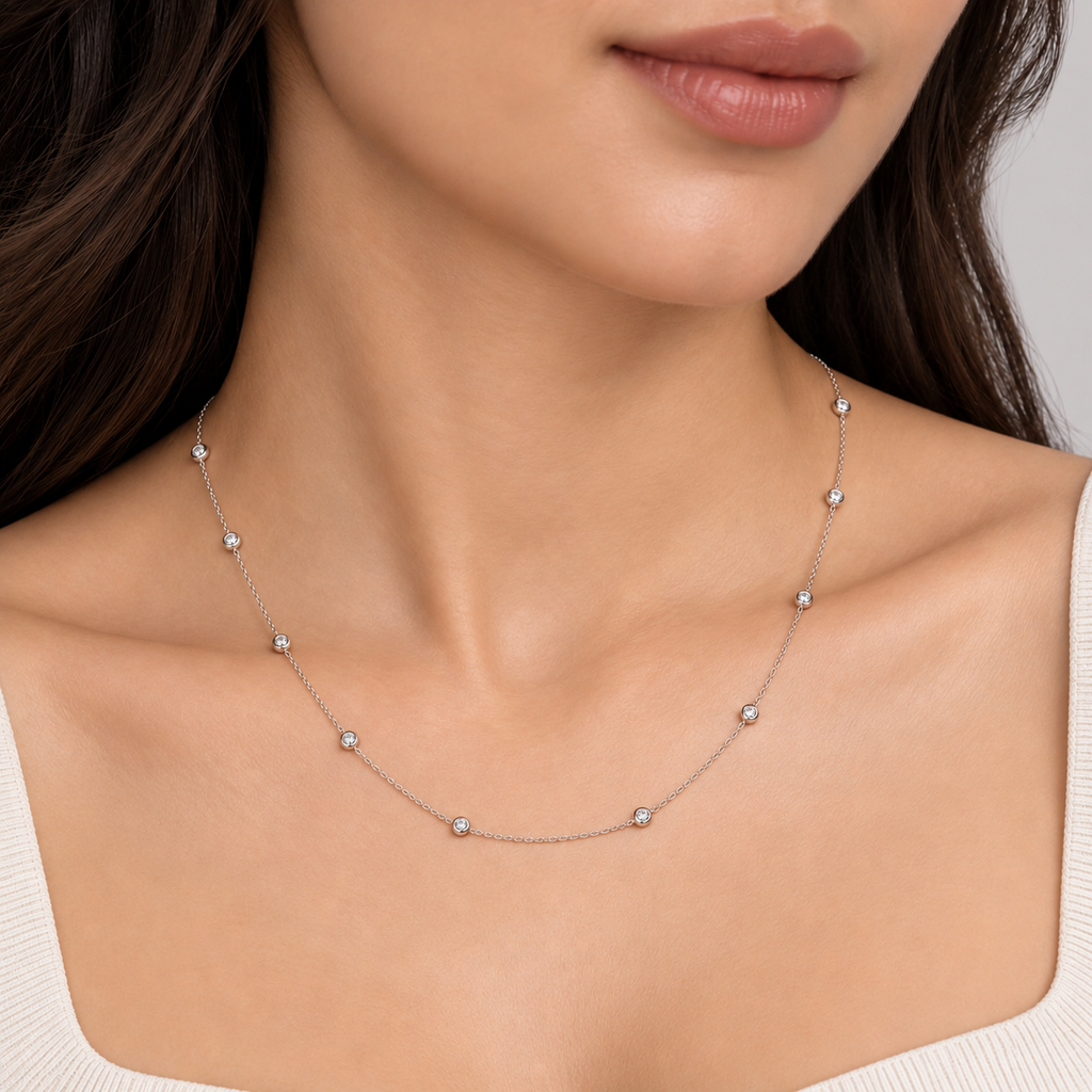A close-up of a model wearing a delicate silver necklace with small, evenly spaced round clear gemstones on a fine chain.