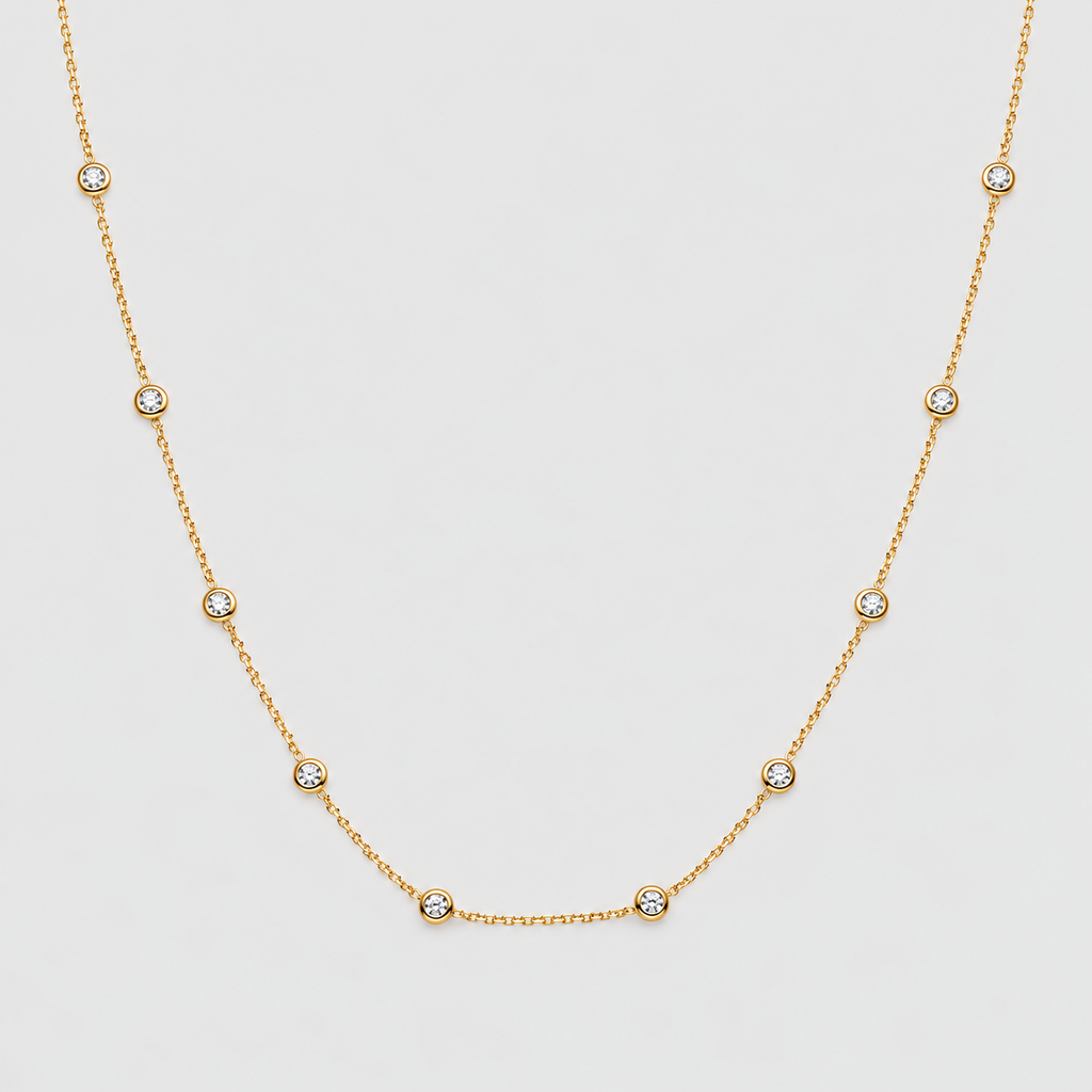 A delicate gold chain necklace featuring seven small, bezel-set round clear gemstones spaced evenly along the chain, displayed against a light gray background.