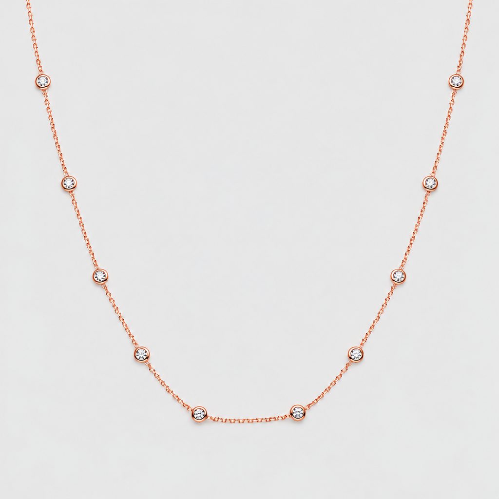 A delicate rose gold necklace featuring a fine chain and small, evenly spaced bezel-set round clear gemstones, displayed on a light gray background.