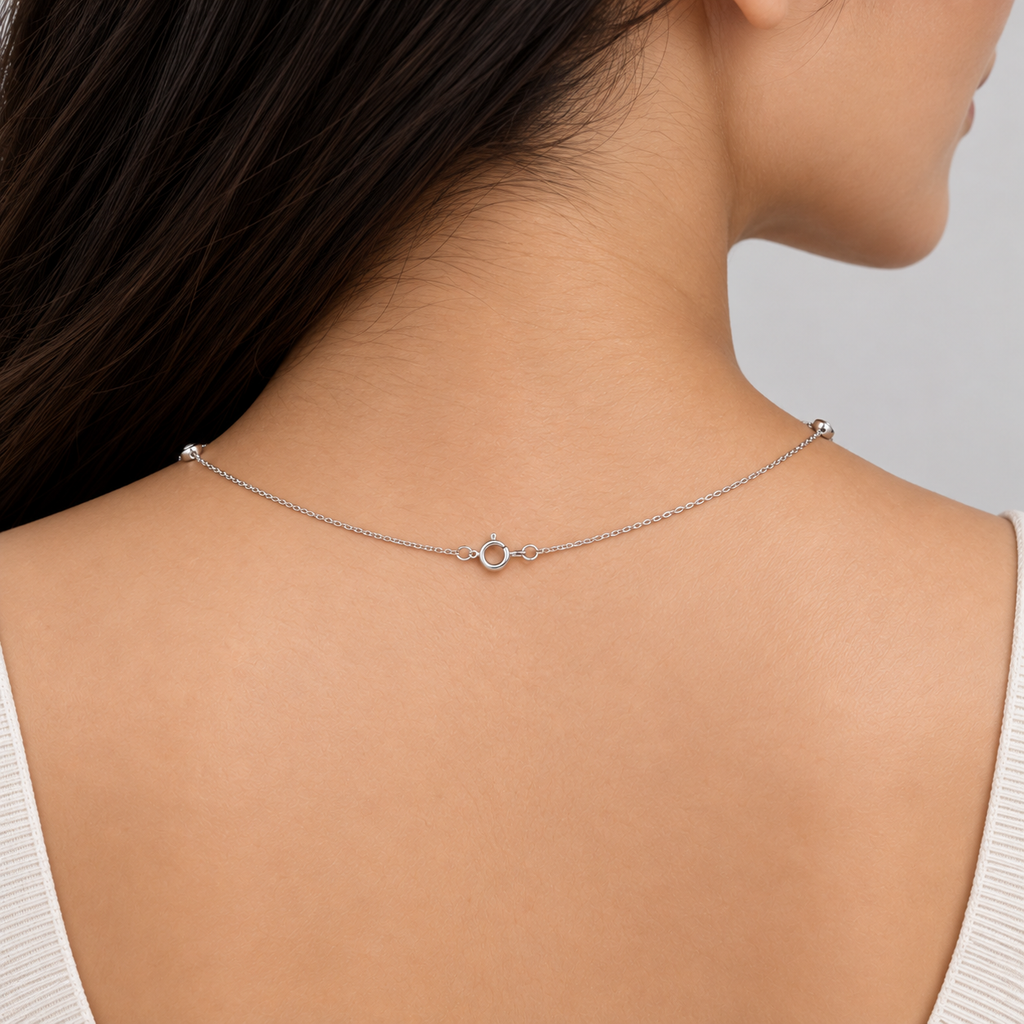 A close-up of a woman's back and neck wearing a delicate silver chain necklace with a small central ring clasp, shown against a light gray background.