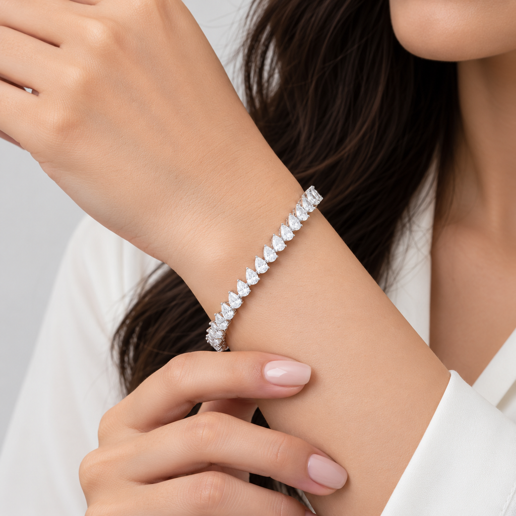 A close-up of a woman's wrist wearing a sparkling silver tennis bracelet with heart-shaped clear stones, styled with a white blouse.