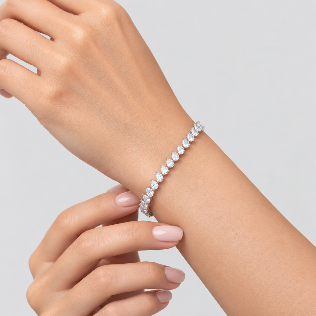 A close-up of a woman's wrist and hand wearing a sparkling tennis bracelet with clear round-cut stones on a light gray background.