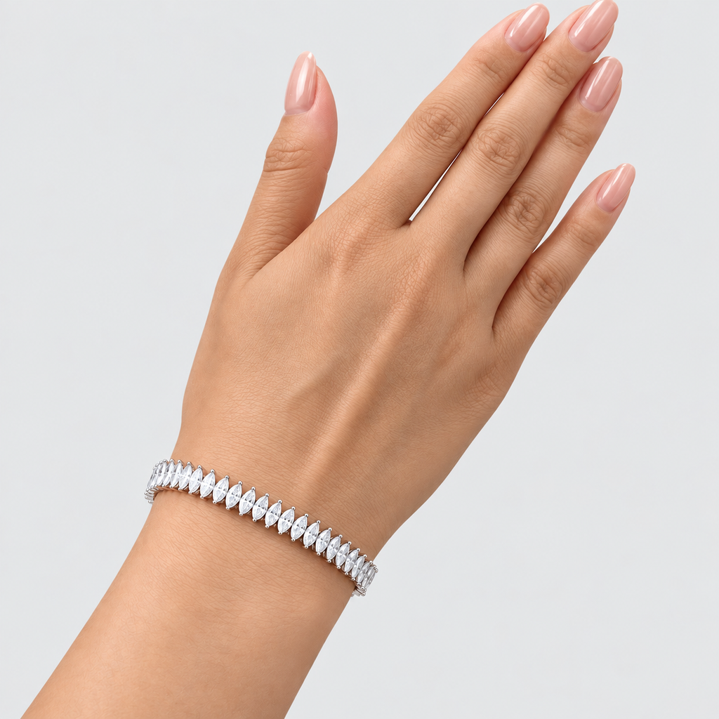 A close-up of a hand wearing a delicate silver tennis bracelet with marquise-cut stones, set against a clean light gray background.