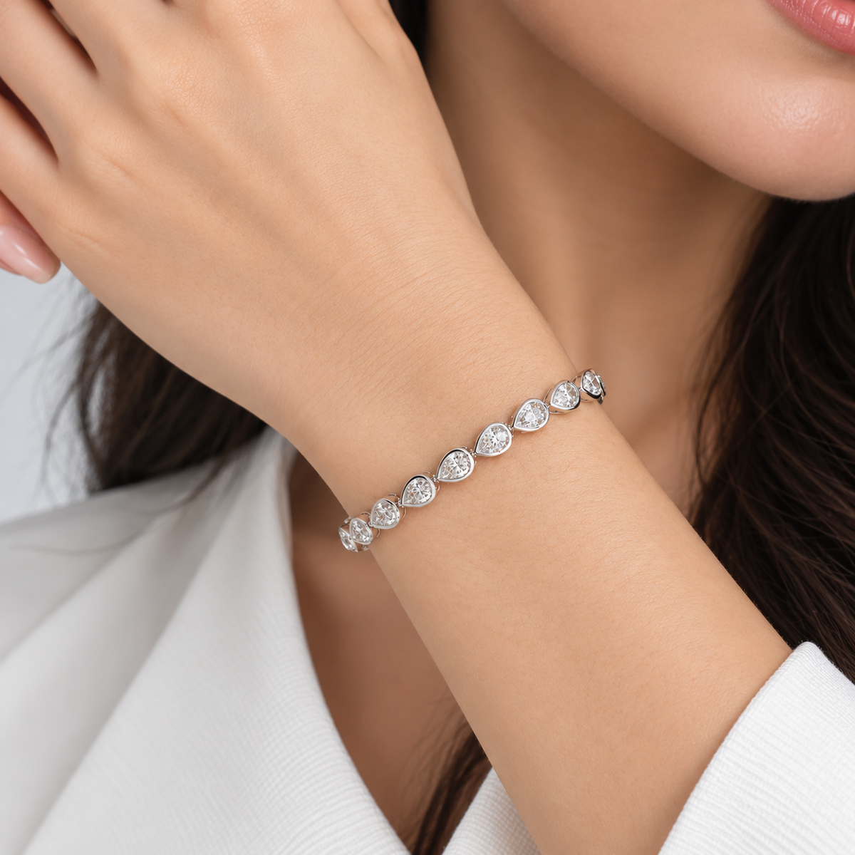 A close-up of a woman's wrist wearing a delicate silver bracelet with a row of clear teardrop-shaped gemstones. The image features soft, professional lighting and a clean, non-distracting background.
