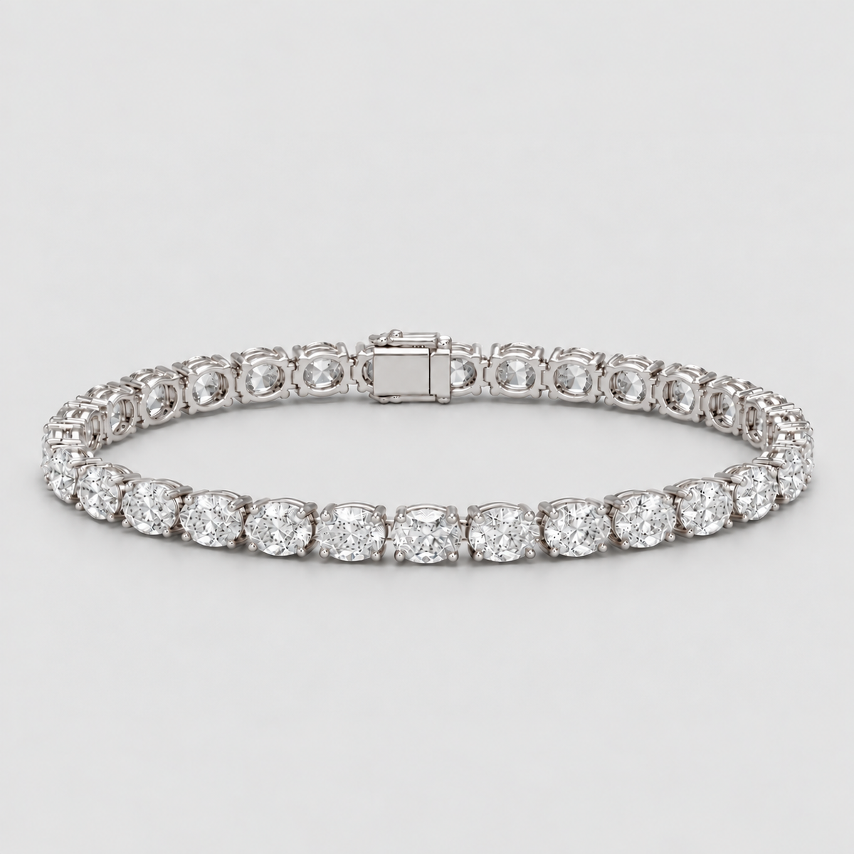 A diamond tennis bracelet in a silver-toned setting, featuring round brilliant-cut diamonds and a rectangular clasp, photographed on a light gray background.