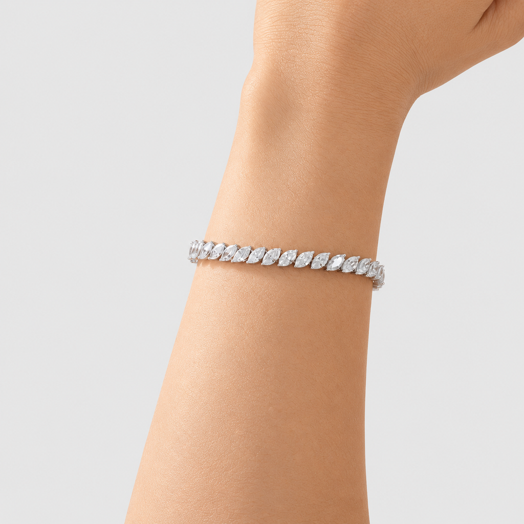 A silver tennis bracelet with marquise-cut clear stones, shown worn on a person's wrist against a light gray background.