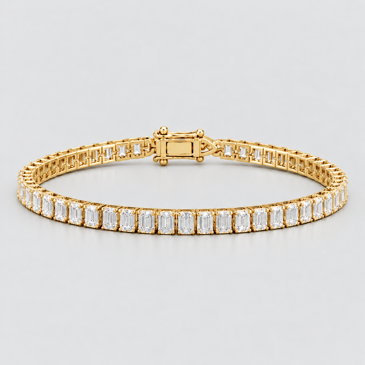 A yellow gold tennis bracelet featuring a continuous row of baguette-cut clear gemstones in a prong setting, shown against a neutral light gray background.