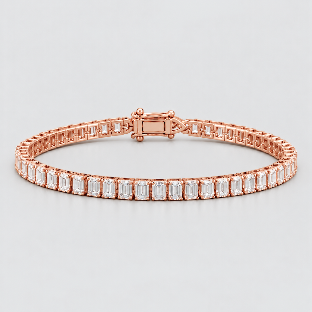 A rose gold tennis bracelet featuring baguette-cut clear stones, displayed on a neutral light gray background.