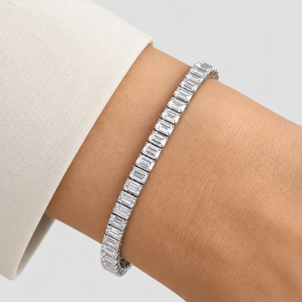 A silver tennis bracelet with baguette-cut clear stones worn on a person's wrist, with a light beige sleeve visible at the side.