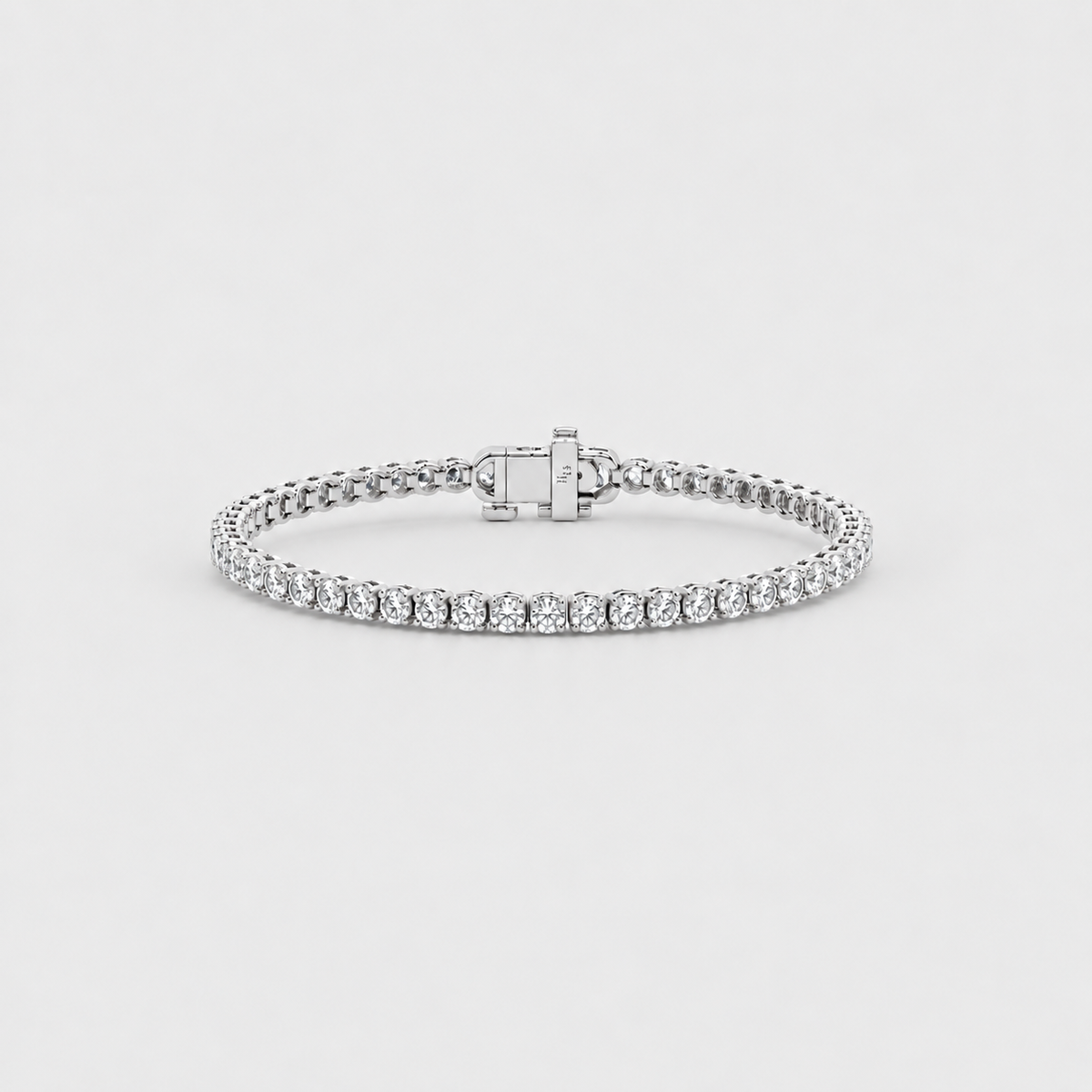 A silver tennis bracelet with a row of round-cut clear stones and a clasp engraved with the brand name  photographed on a light gray background.